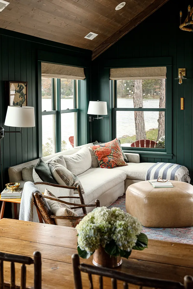 Living room with sectional sofa, ottoman, wooden table, decorative pillows, and windows overlooking water.