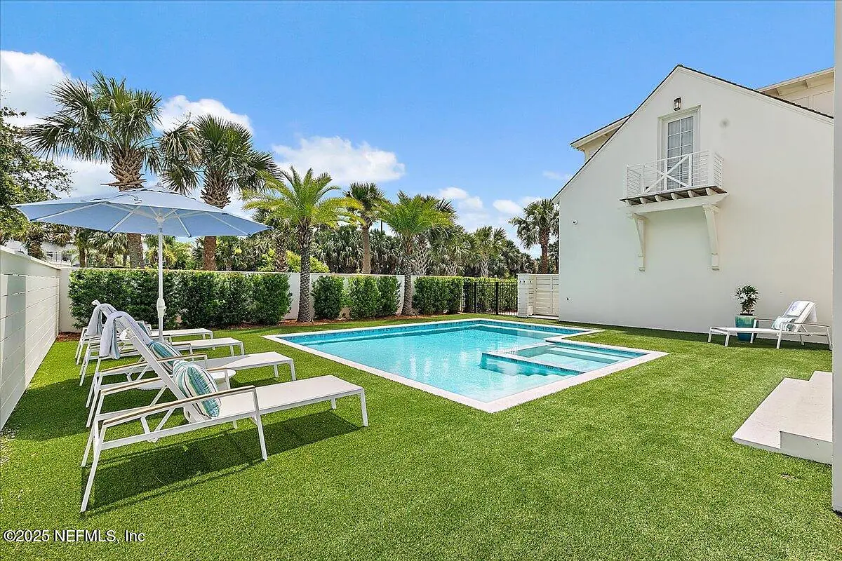 Garden area with swimming pool, white lounge chairs, umbrella, and palm trees.