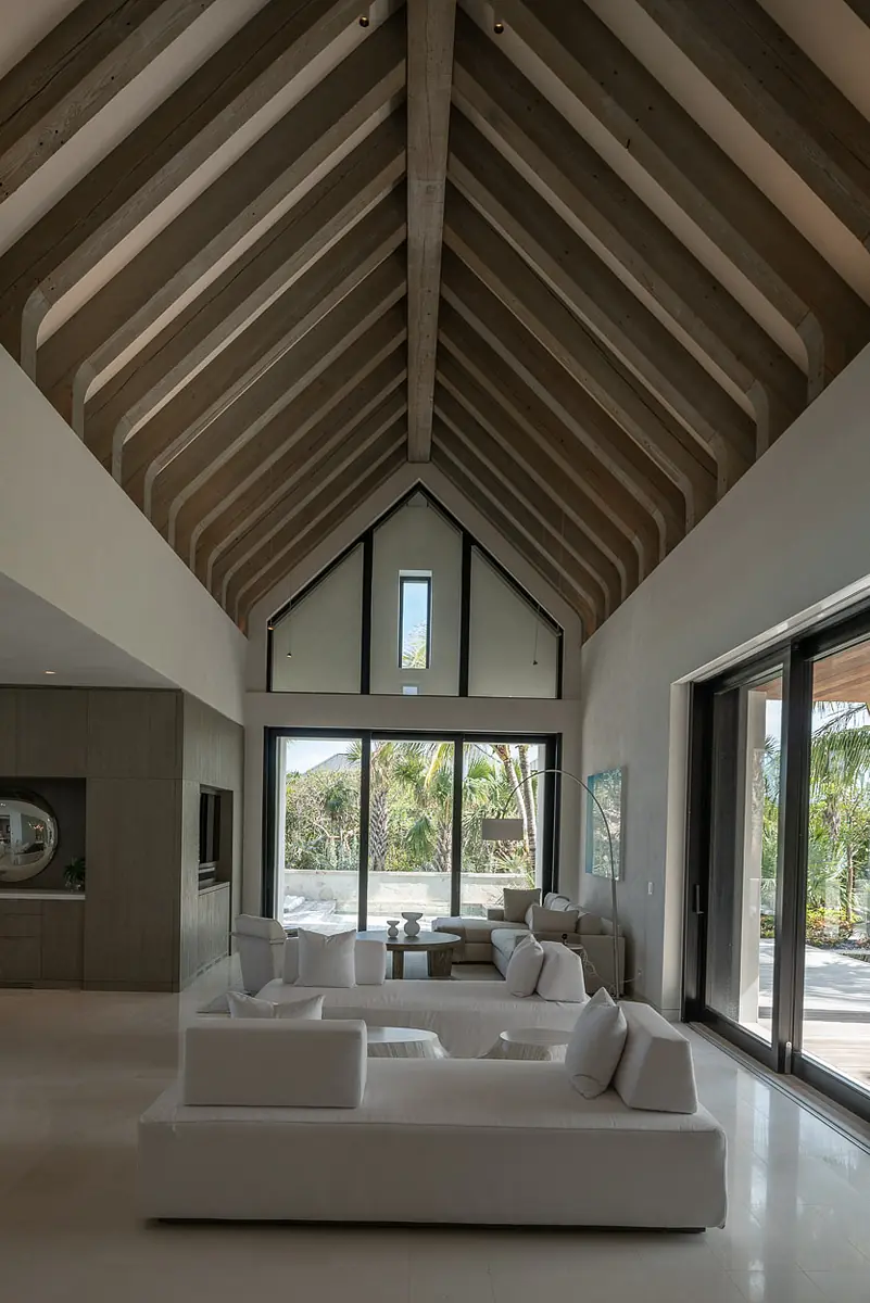 Living room with white sectional sofa, wooden coffee table, large glass doors, and exposed wooden beams