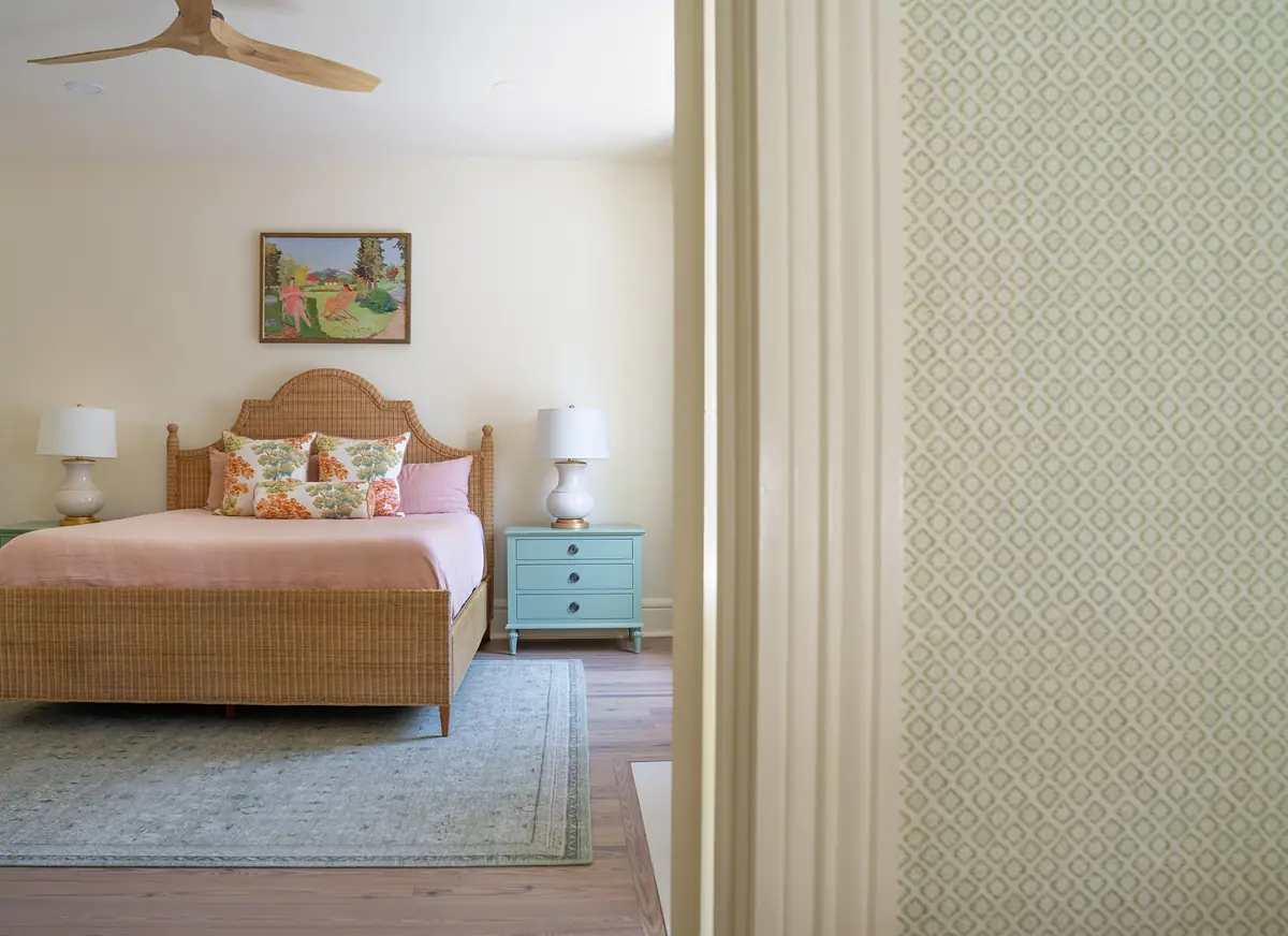 Bedroom with rattan headboard bed, nightstands, lamps, area rug, and a wall painting.