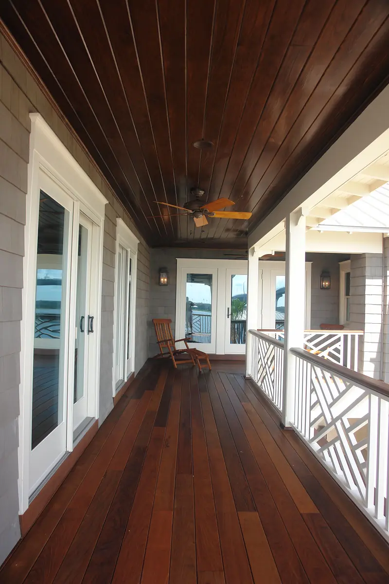 Deck with wooden floor, ceiling, rocking chair, three doors, vertical railings, and ceiling fan.