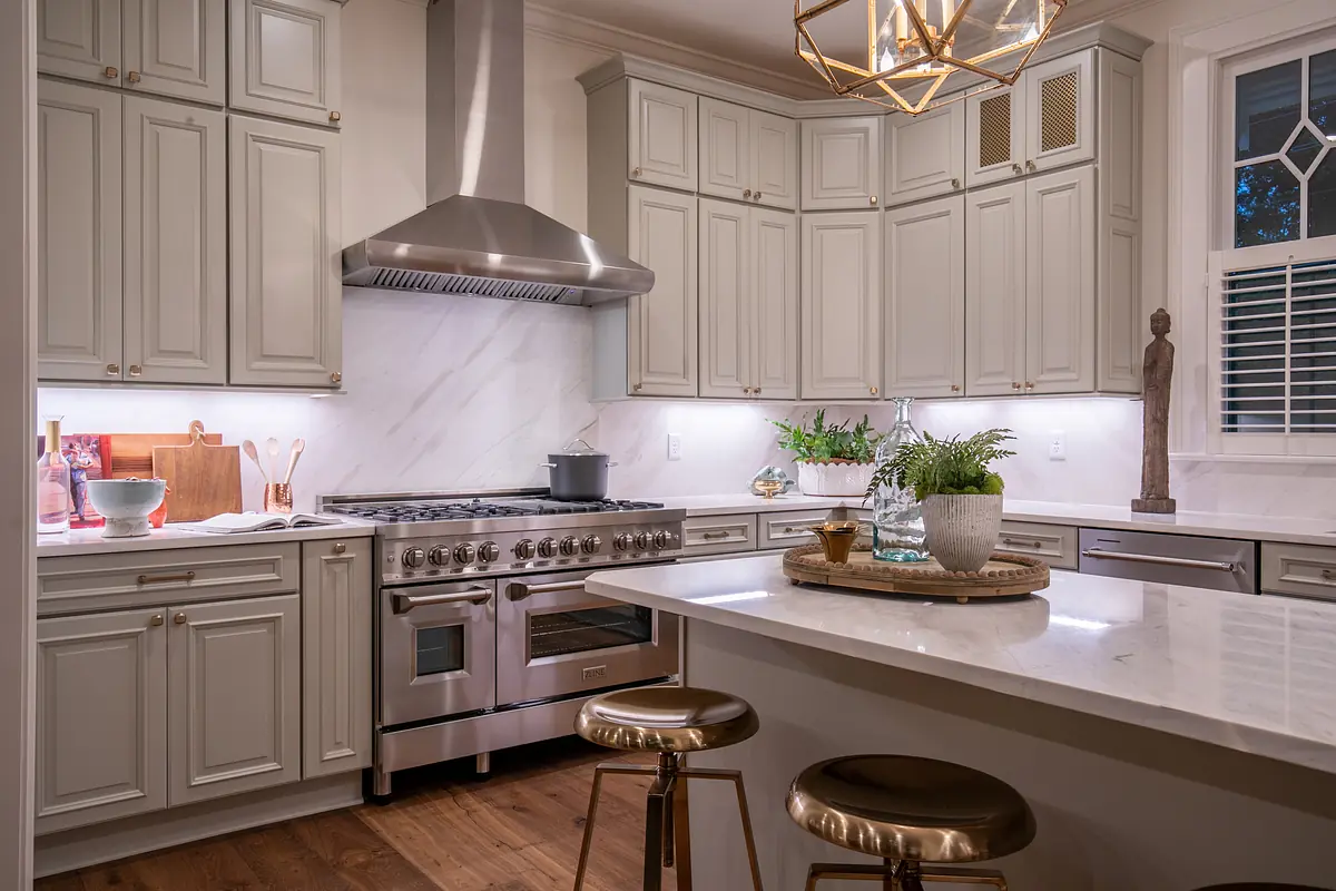 Kitchen with white cabinetry, marble countertop, stainless steel appliances, and kitchen island with bar stools.