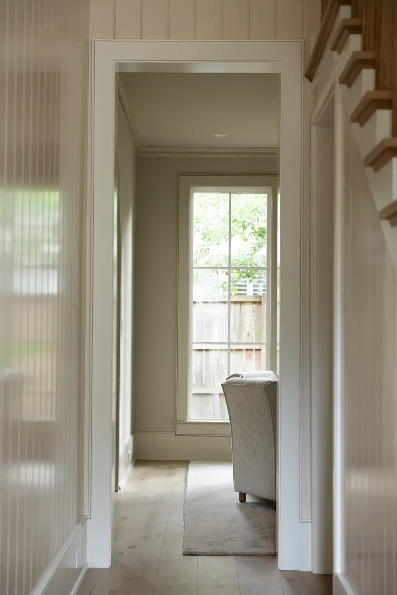 Hallway with walls, large window, beige chair, rug, crown molding, and wooden staircase.