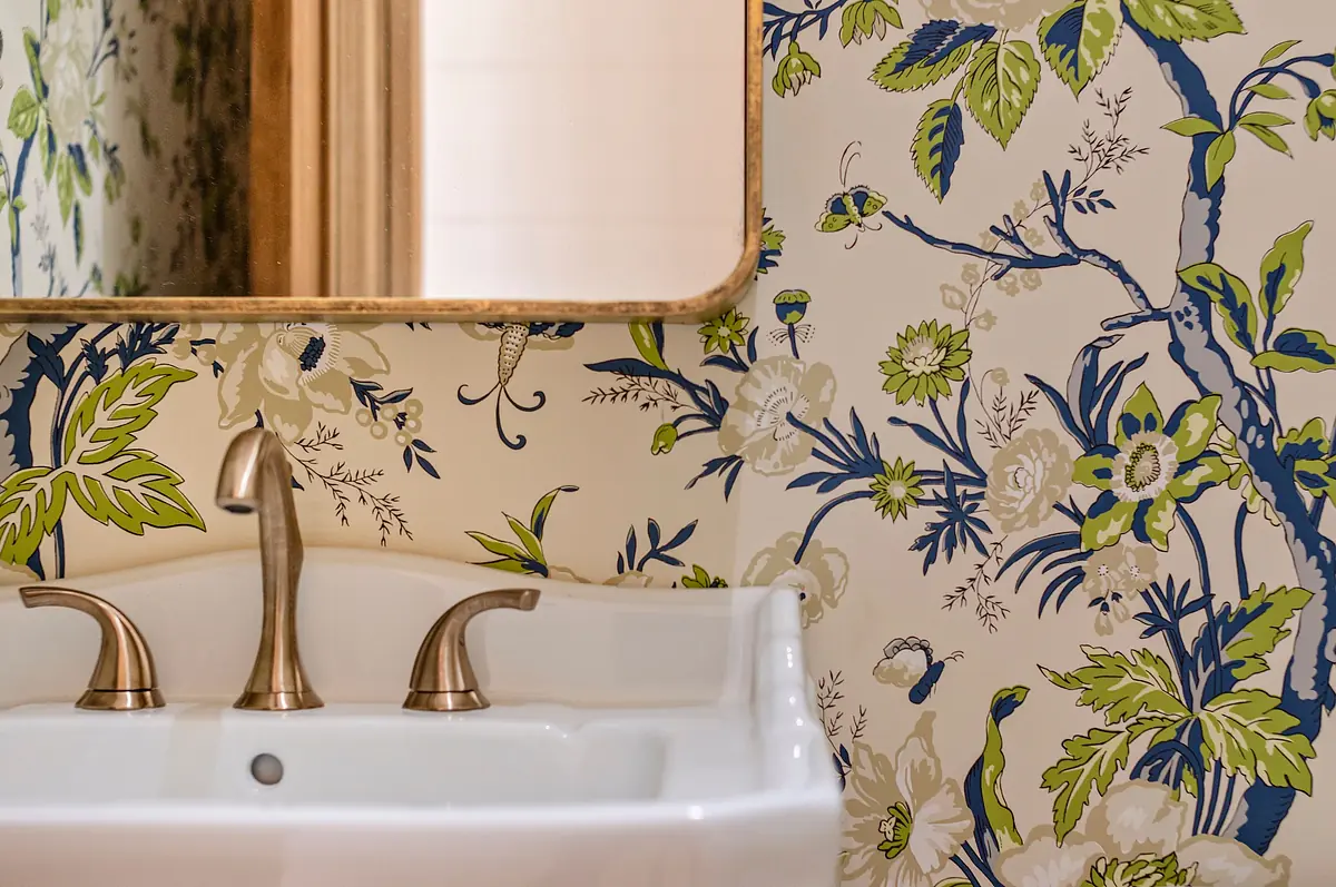 Bathroom with white sink, bronze faucets, floral wallpaper, and gold-framed mirror.