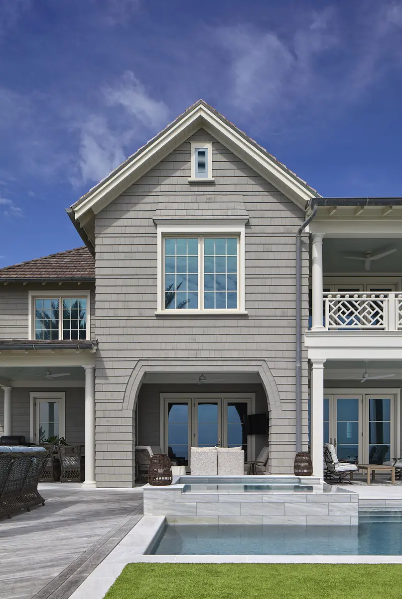 Exterior rear view with gray siding, large windows, sliding glass door, patio, swimming pool, and grass.