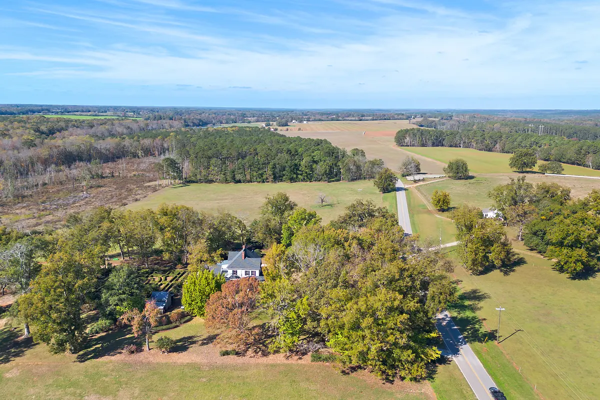 Aerial view of a rural landscape with a house, trees, and fields.