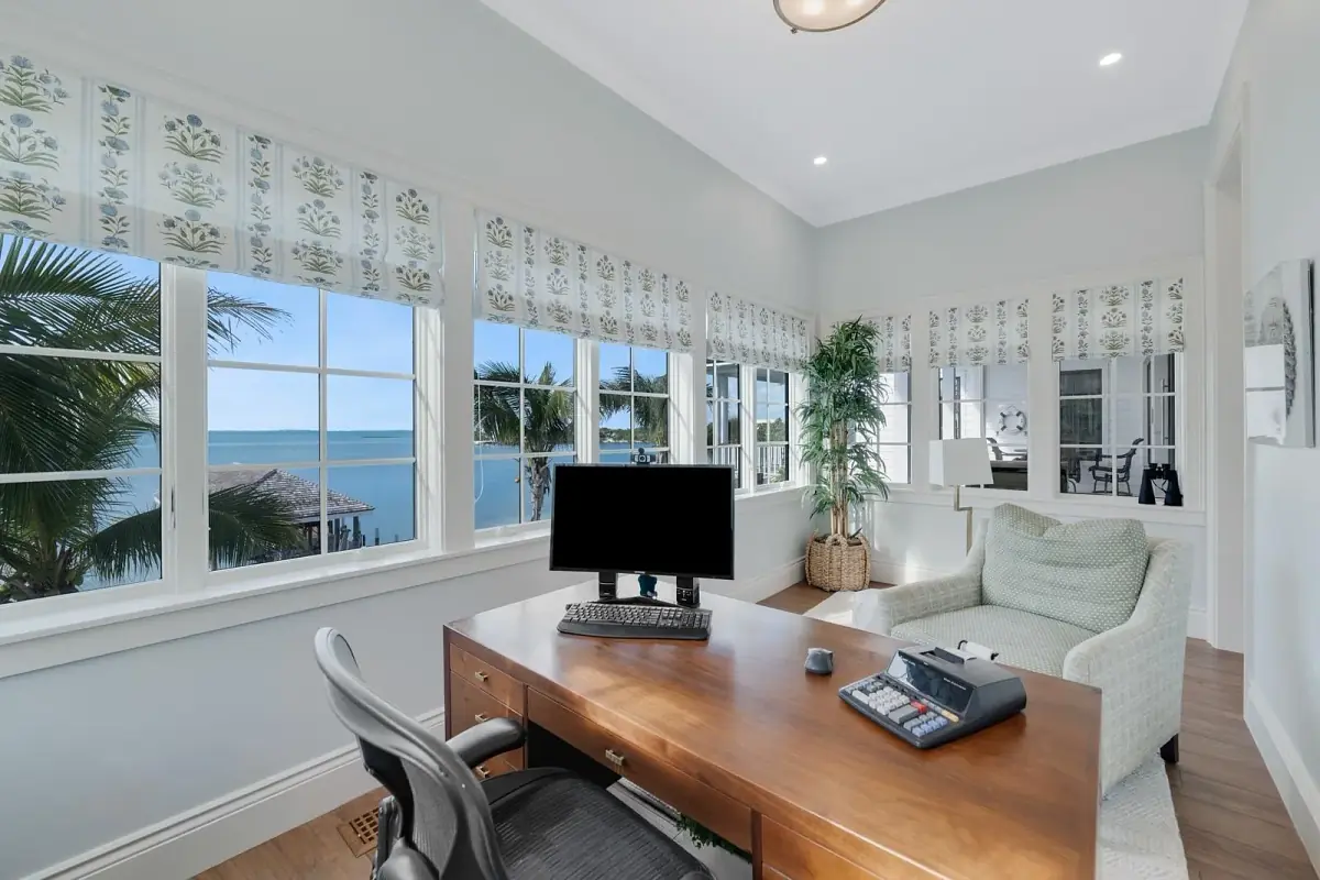 Office with wooden desk, ergonomic chair, computer, armchair, and large windows with sea views.