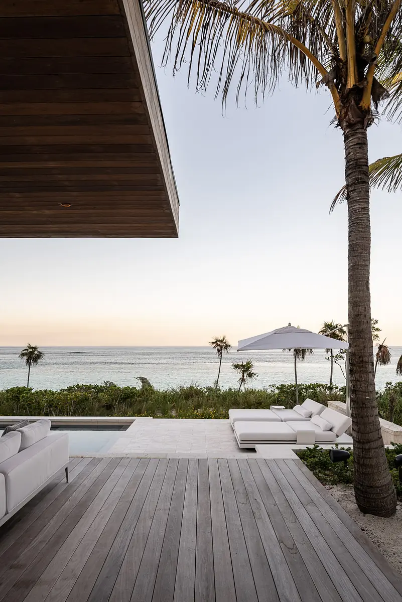 Outdoor deck with white sectional sofa, lounge chair, umbrella, wooden planks, and ocean views