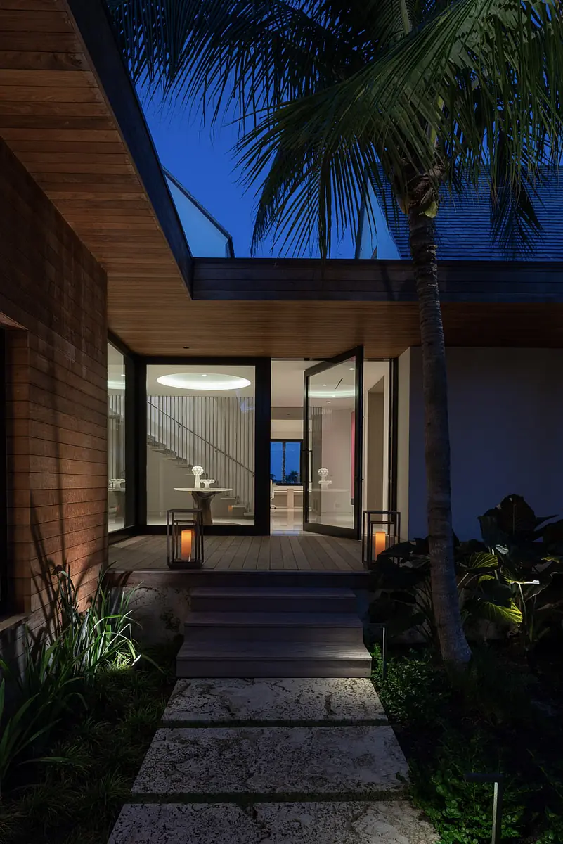 Exterior front with stone pathway, glass door, wooden paneling, lanterns, and surrounding plants.