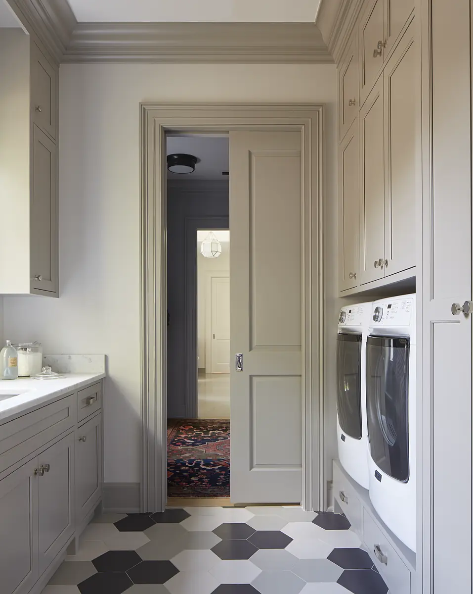 Laundry room with gray cabinetry, marble countertop, front-loading washers, and hexagonal black and white tiles.