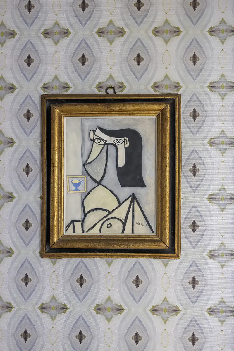 Framed abstract artwork on patterned wallpaper with geometric design in neutral tones.