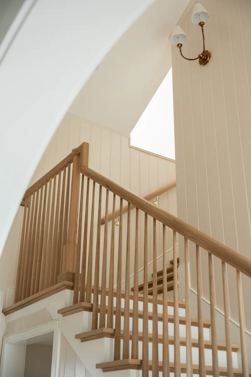 Staircase with wooden banisters, shiplap walls, and wall-mounted light fixture near skylight