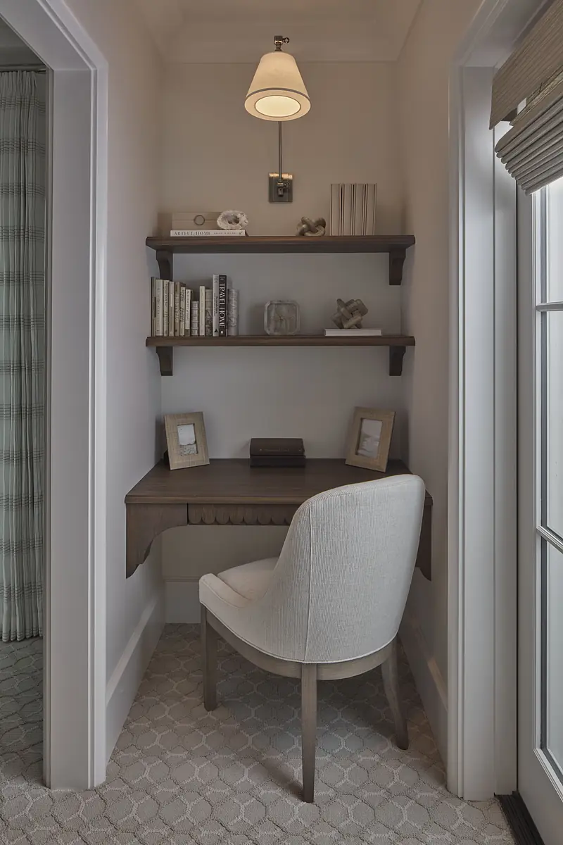 Small office with wooden desk, white chair, floating shelves, and wall sconce.