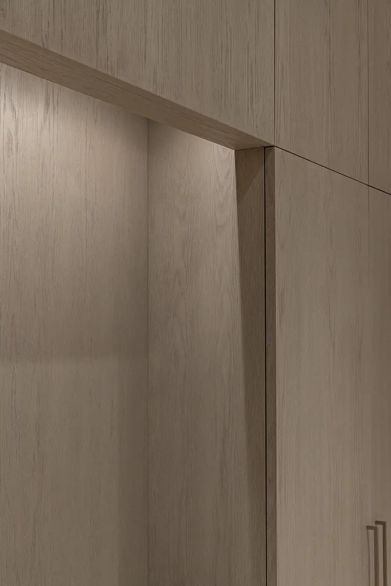 Close-up of wooden cabinetry with textured surface, minimalist handles, and soft indirect lighting