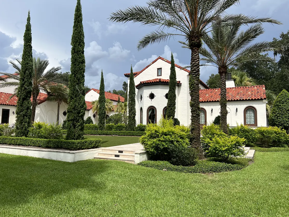 Exterior front view of a house with white stucco, red tile roof, arched windows, and landscaped lawns.