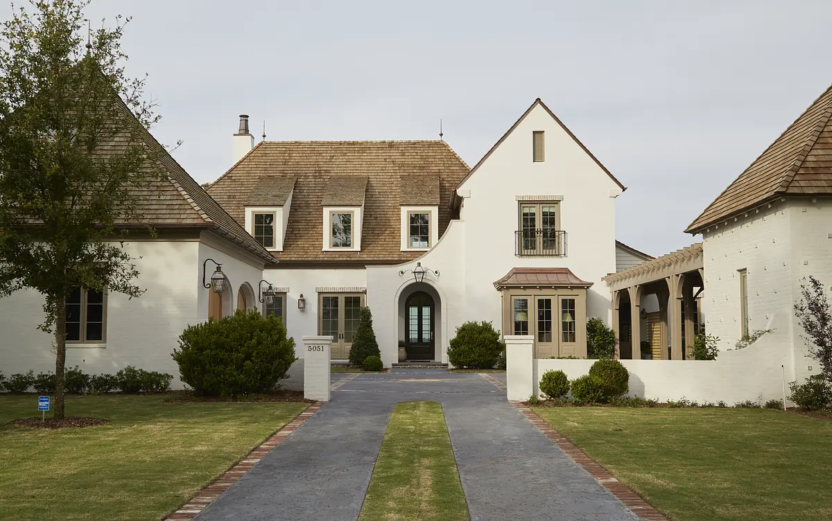 Front exterior of a house with central entrance, gabled roofs, stucco walls, and landscaped pathway.