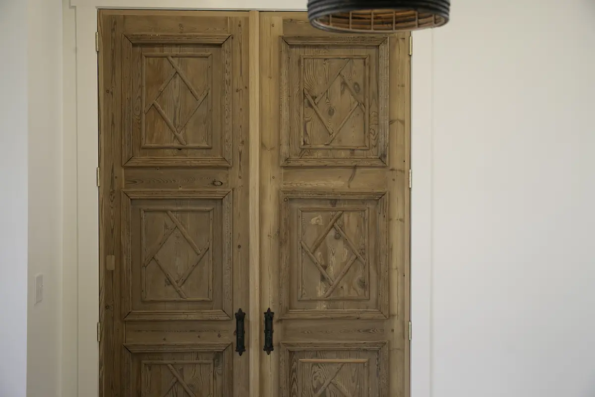 Foyer with large wooden double doors and a decorative ceiling light fixture against white walls.