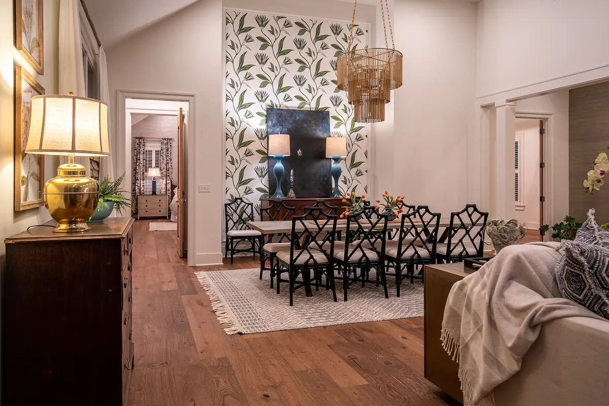 Dining room with dark wood table, black chairs, wall mirror, leaf-patterned wallpaper, and table lamp.