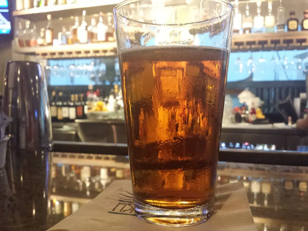 Bar scene with amber beverage on granite countertop, shelves of bottles, and a cocktail shaker.