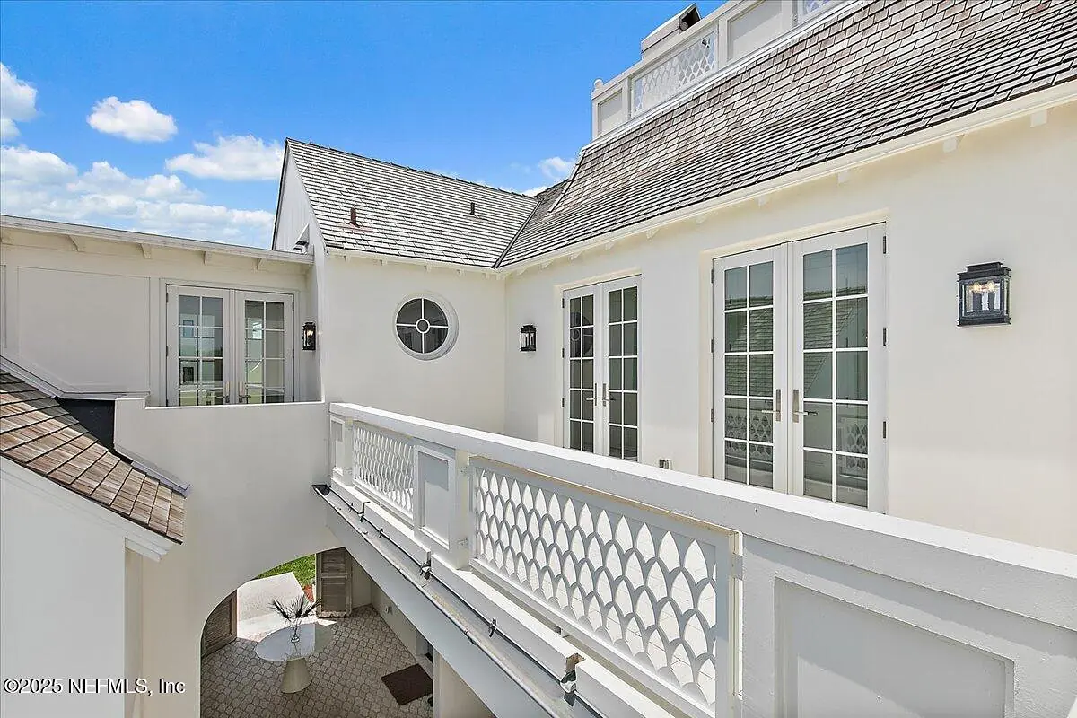 Exterior rear view with balcony, double doors, windows, and a table with chairs