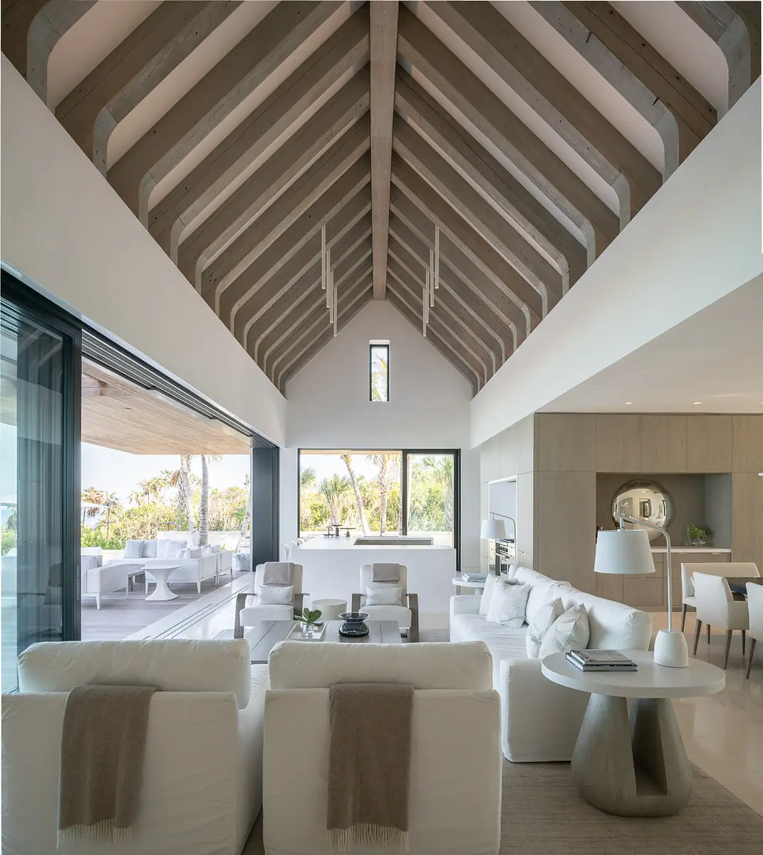 Living room with white sectional sofa, round table, large windows, exposed beams, and integrated fireplace.