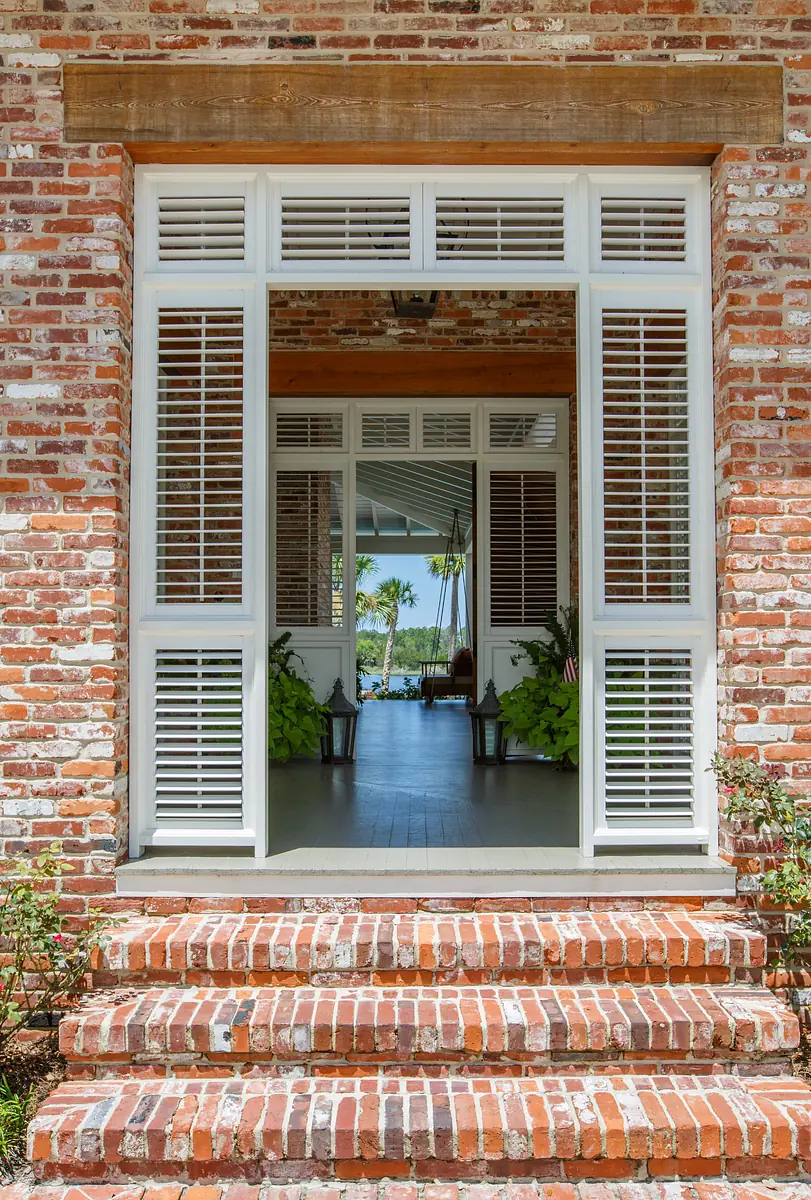 Exterior front view with brick steps, white shutters, and a doorway leading to a covered porch.