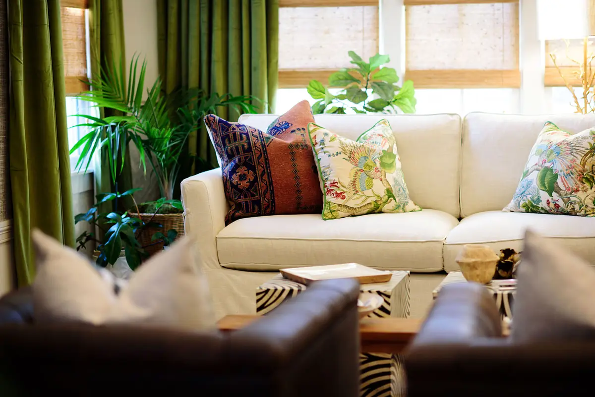 Living room with white sofa, brown leather chairs, coffee table, plants, green curtains, and animal print rug.