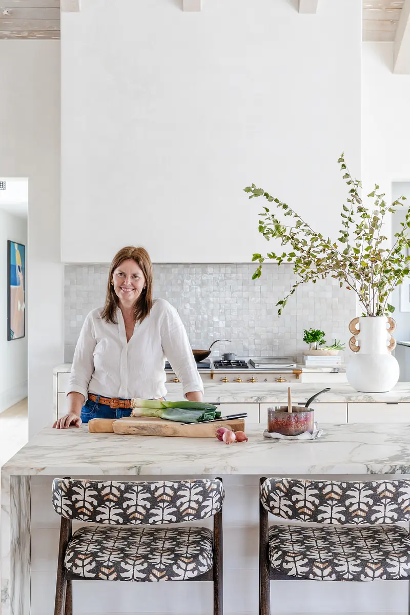 Kitchen with marble island, patterned stools, white cabinetry, and a vase with greenery on display.