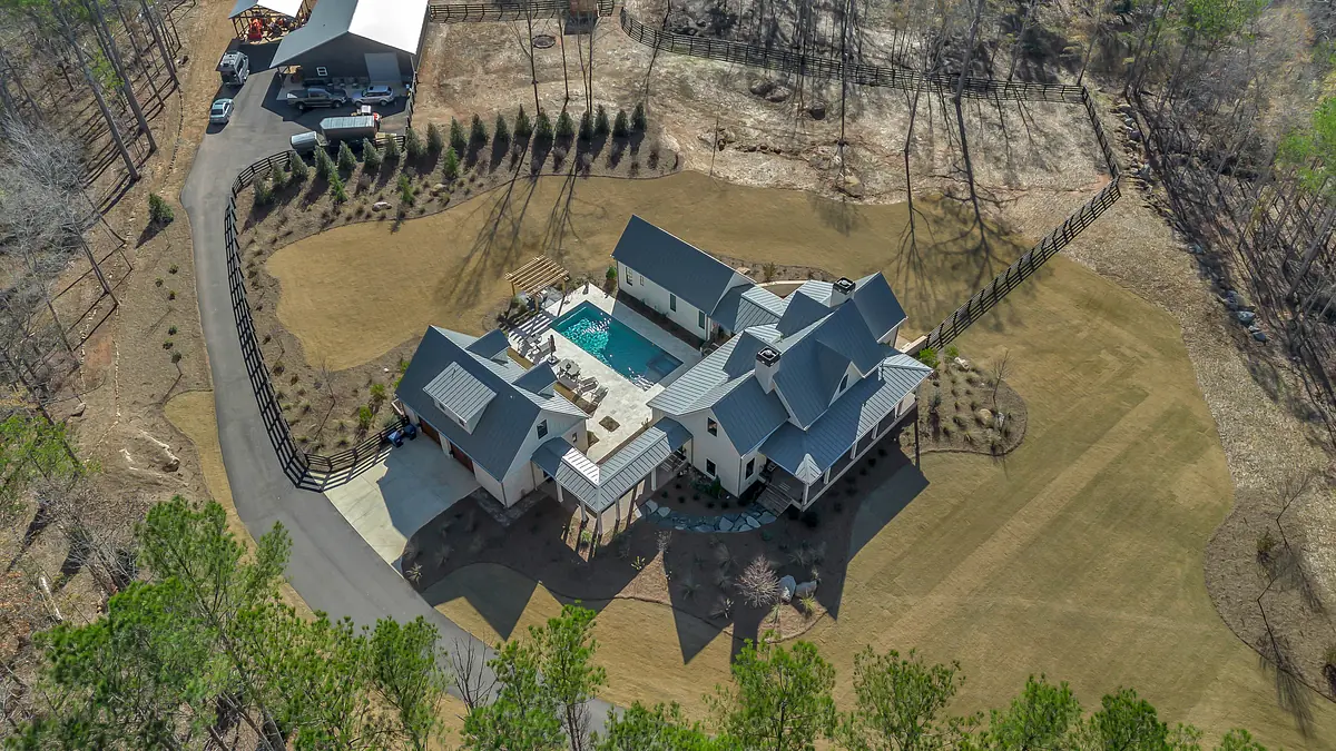 Aerial view of a house with a pool, landscaped yard, and circular driveway surrounded by a wooden fence.