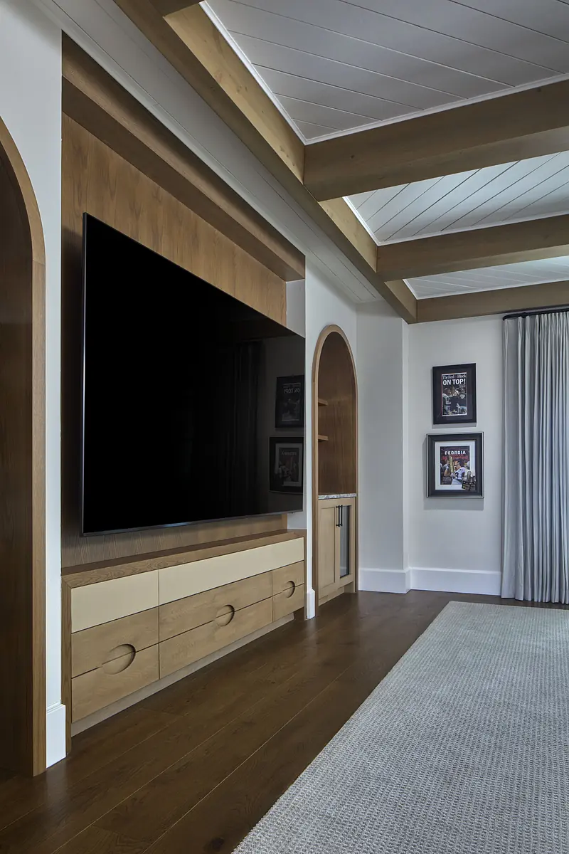Living room with a flat-screen TV, wooden wall unit, rug, and framed pictures on light-colored walls.