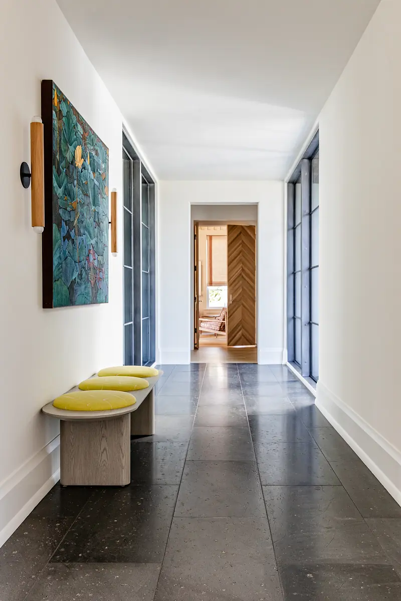 Hallway with stone floor, yellow benches, wall art, and glass doors leading to adjacent rooms.