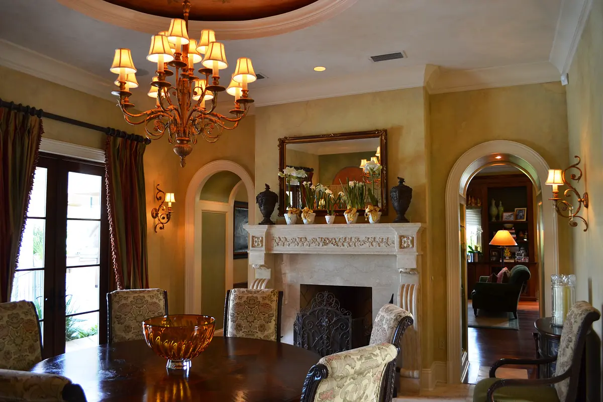 Dining room with round table, upholstered chairs, chandelier, sconces, and a fireplace with decorative vases