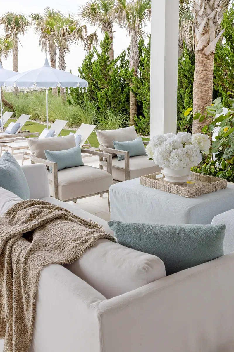 Patio with white sofa, blue cushions, coffee table, lounge chairs, and palm trees in the background