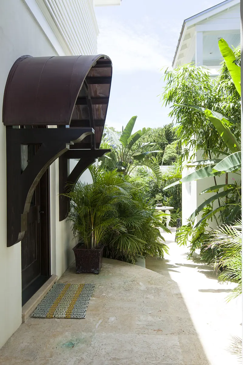 Exterior front area with curved awning, wooden door, stone pathway, plants, and patterned doormat