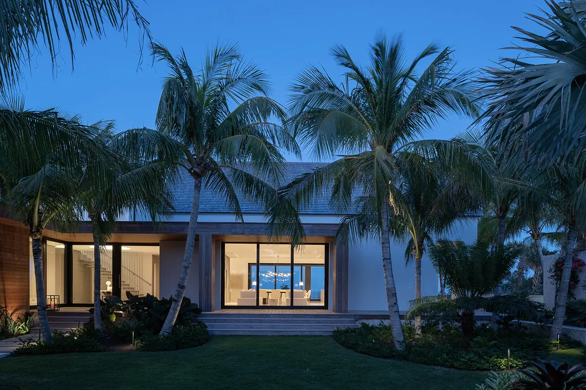 Exterior view of house with palm trees, glass sliding doors, wooden accents, and manicured landscaping.
