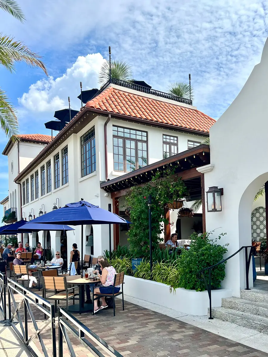 Restaurant exterior with tiled roof, large windows, outdoor seating, and decorative plants.