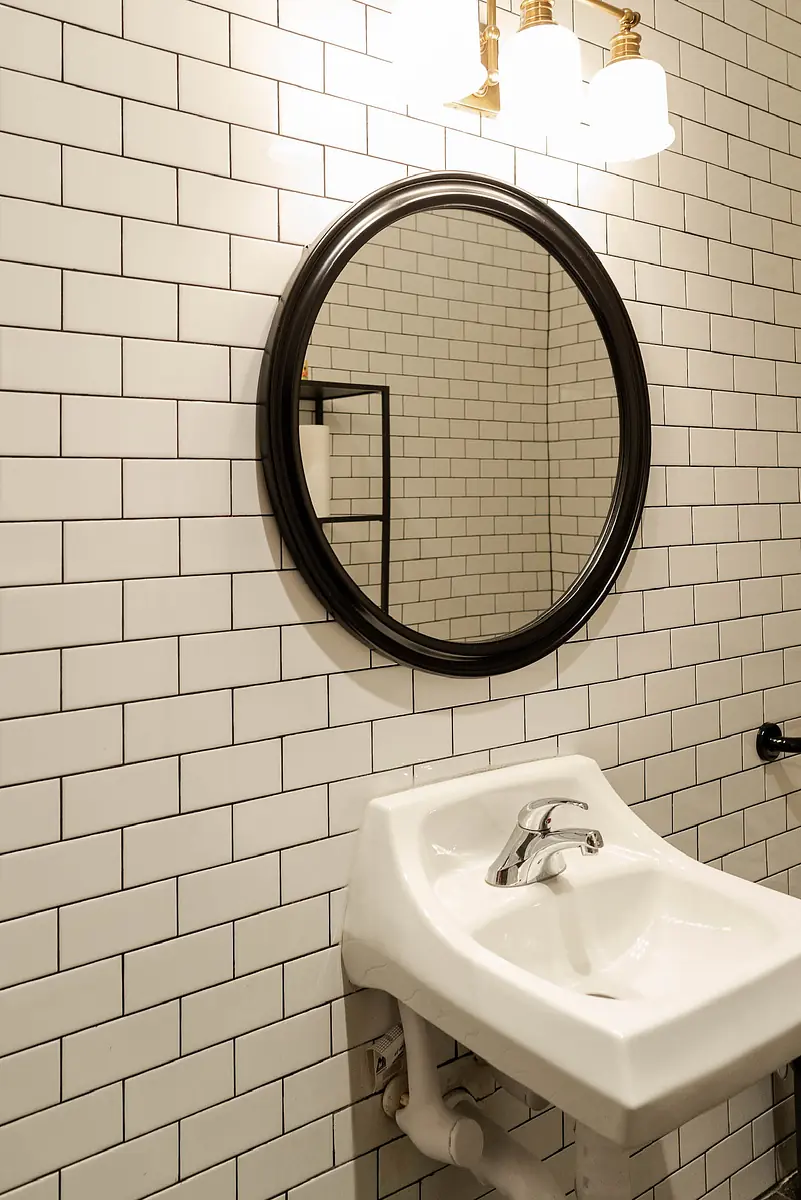 Bathroom with white sink, round mirror, subway tile walls, and light fixture above mirror