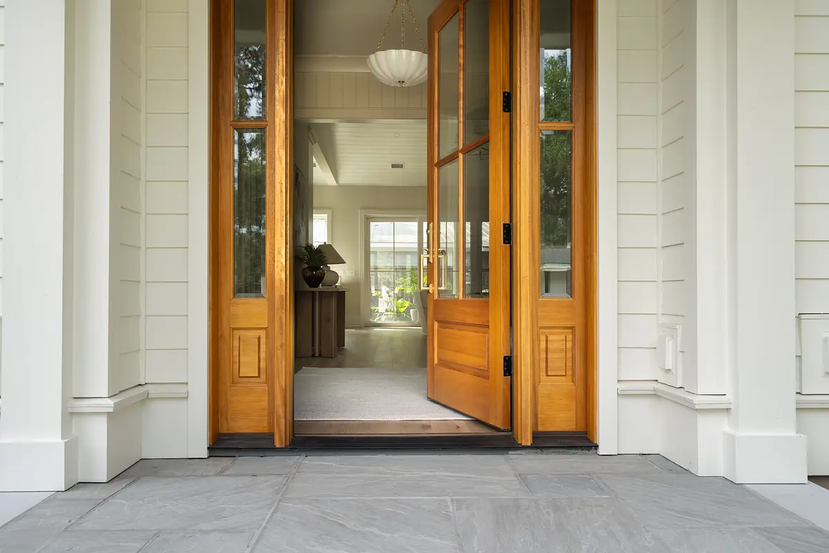 Foyer with double wooden doors, gray tile floor, and round ceiling fixture leading to a well-lit interior.