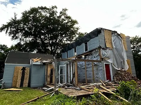 Exterior view of a partially constructed building with boarded windows and a red door.
