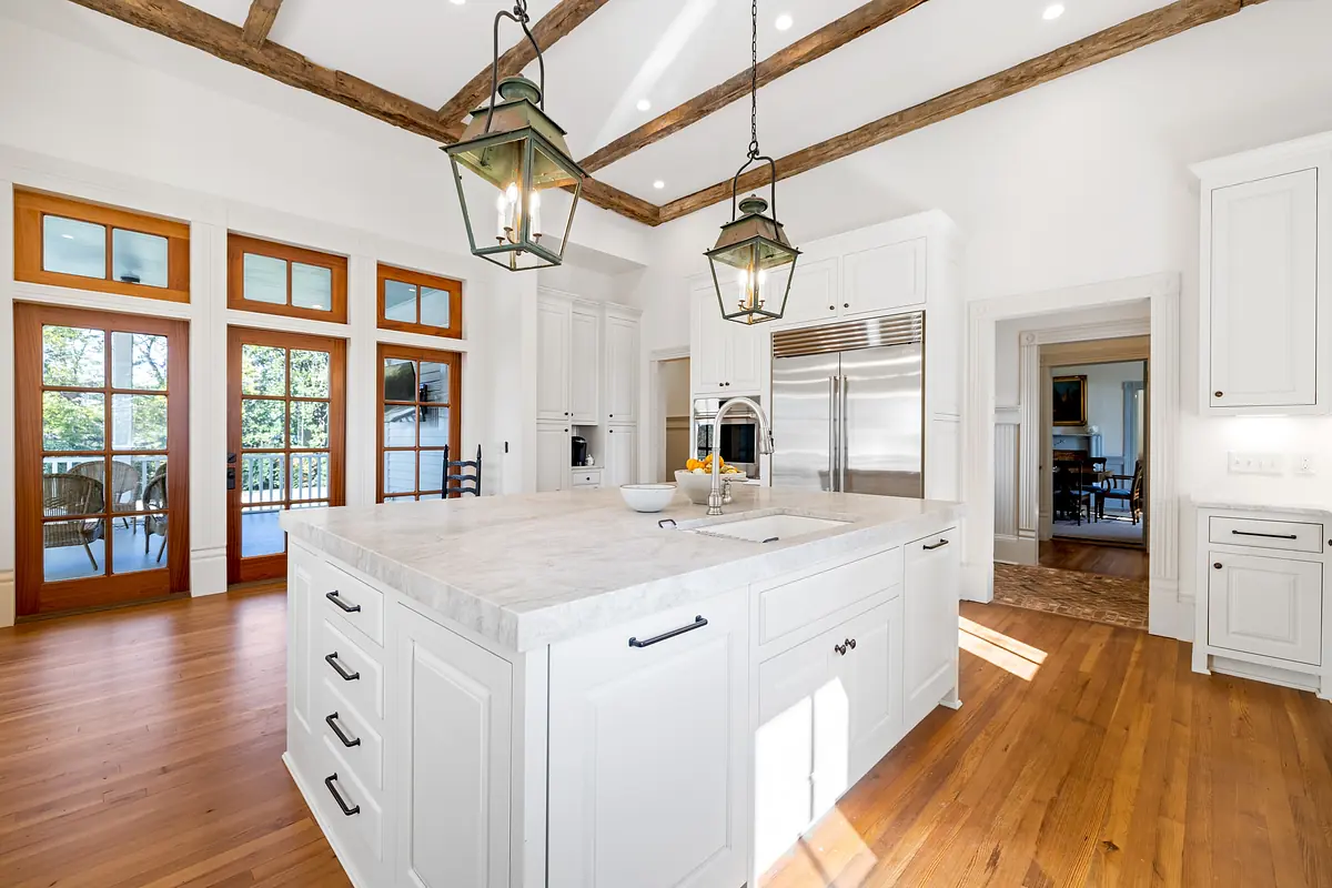 Kitchen with marble island, white cabinetry, stainless steel appliances, and exposed wooden beams.