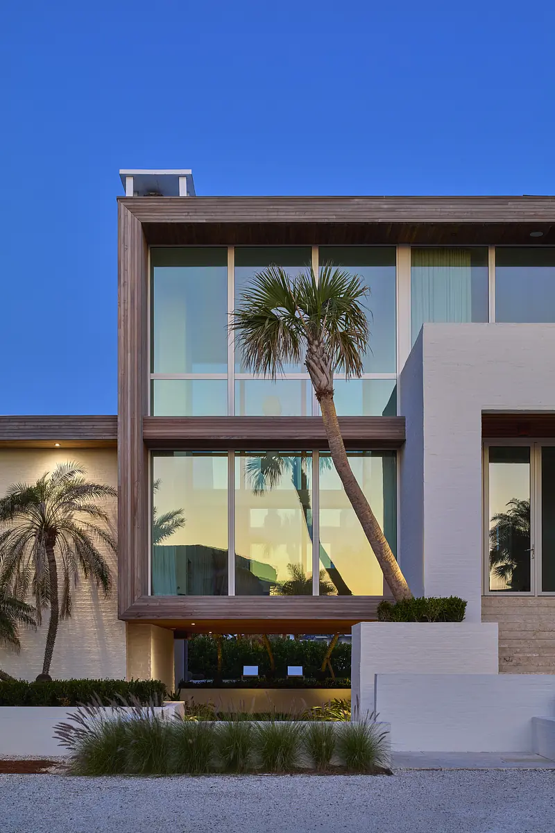 Modern house exterior with large windows, wooden accents, palm tree, and landscaped greenery