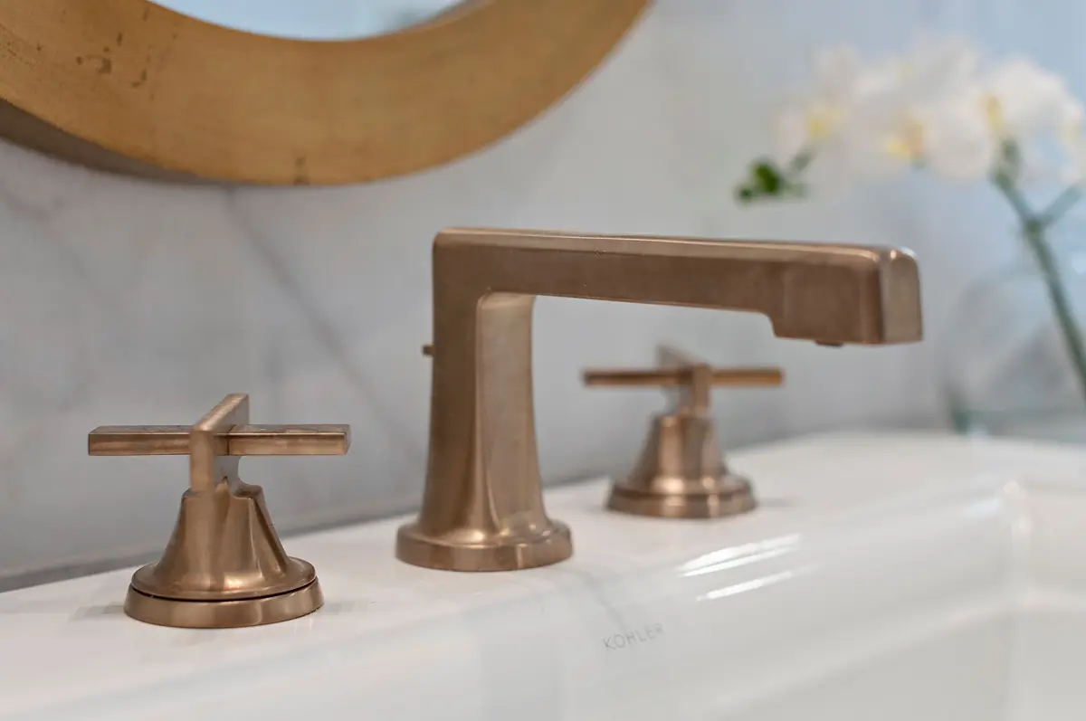 Bathroom with white bathtub, bronze faucet, marble wall, round mirror, and orchid plant