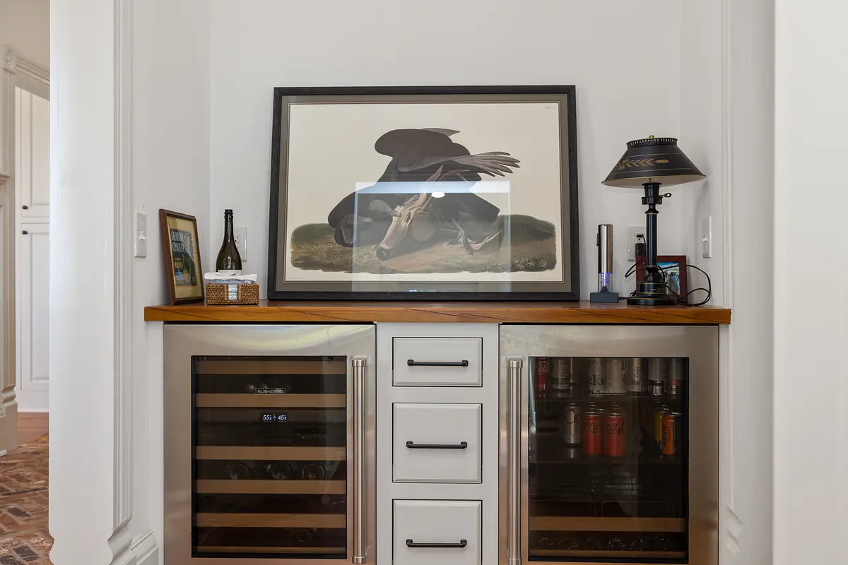 Butler's pantry with wine refrigerators, wooden countertop, artwork, table lamp, and cabinetry.