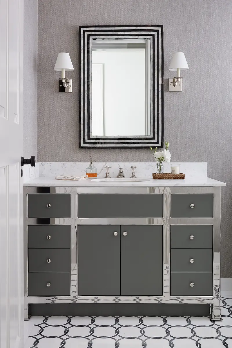 Bathroom with gray vanity, marble countertop, large mirror, wall sconces, and black and white tiled floor