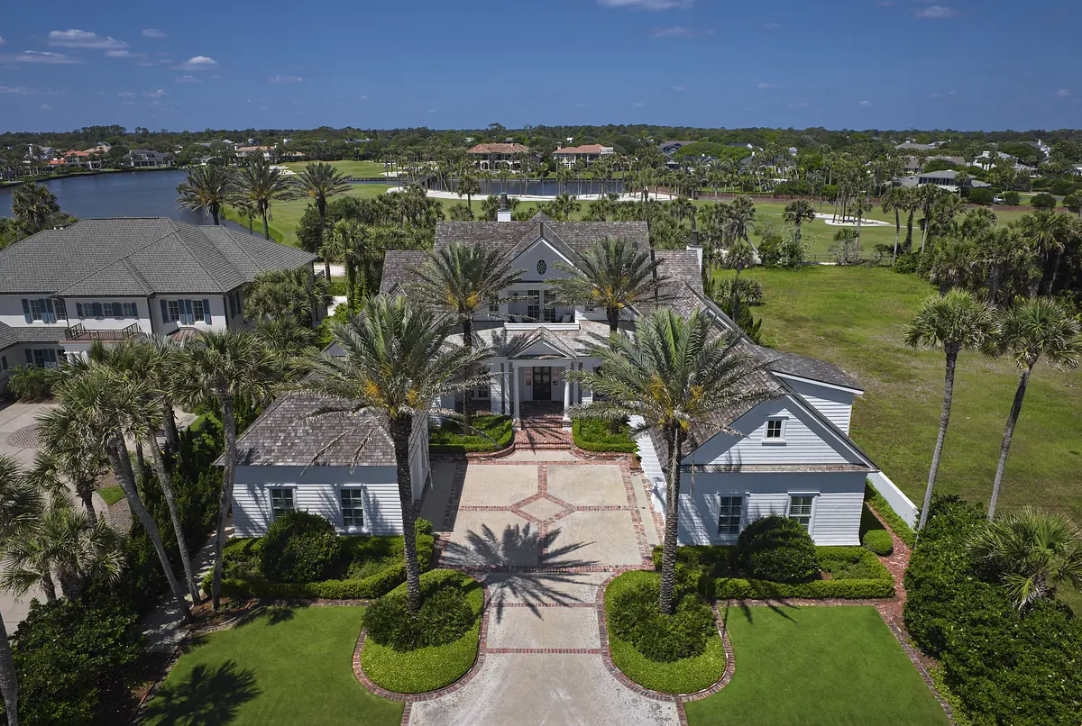Front exterior with driveway, palm trees, landscaped gardens, multi-gabled roof, and stone pathway.