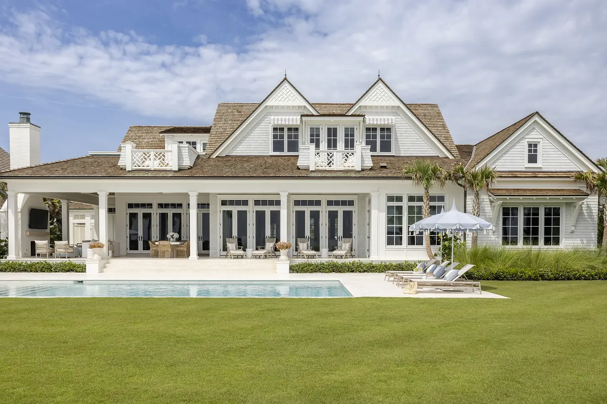 Exterior rear view with swimming pool, patio, landscaped lawn, and a house with gabled roofs and large windows.
