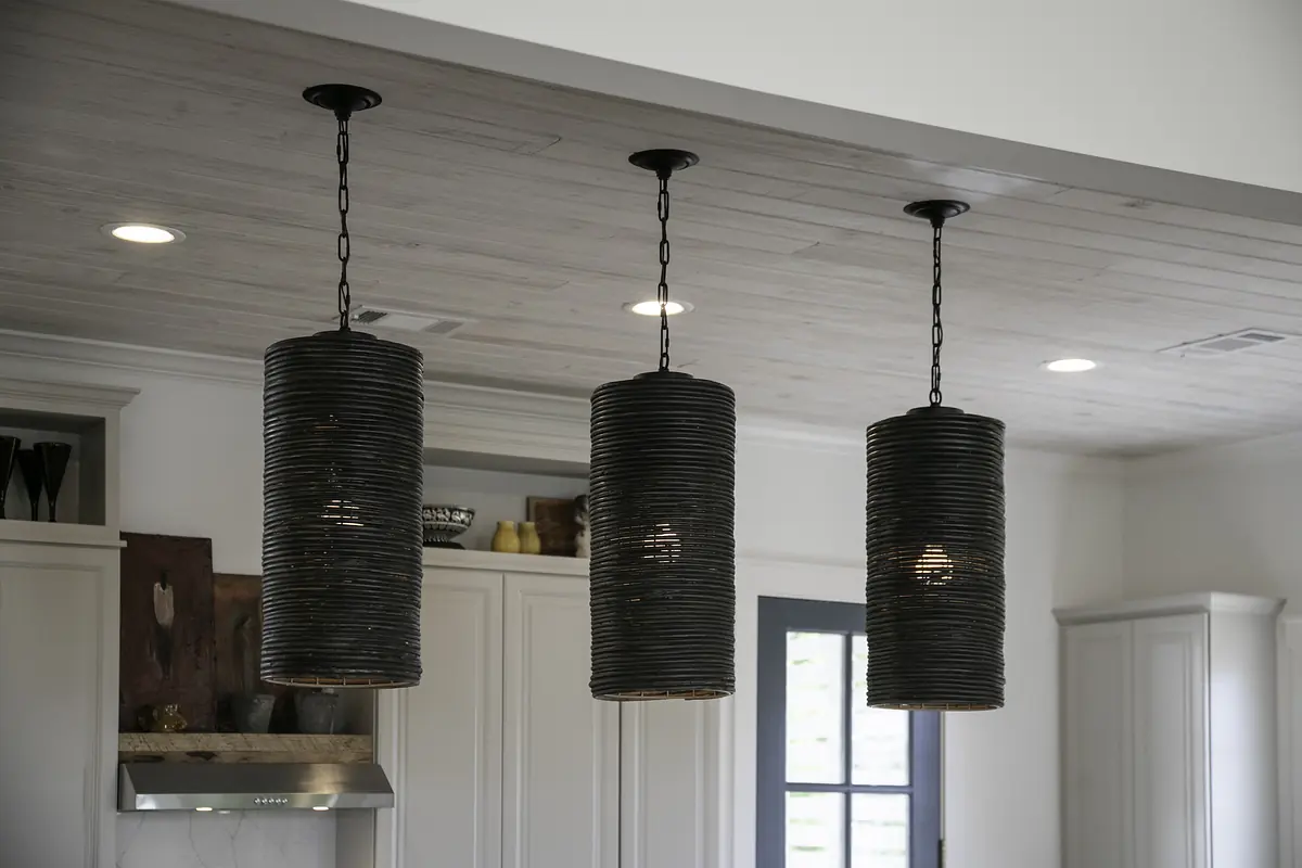 Kitchen with three pendant lights, white cabinetry, and dark countertop under wood panel ceiling.