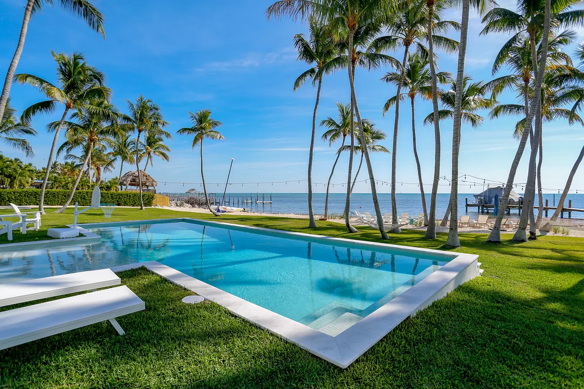 Outdoor area with swimming pool, palm trees, ocean view, dock, and lounge chairs.