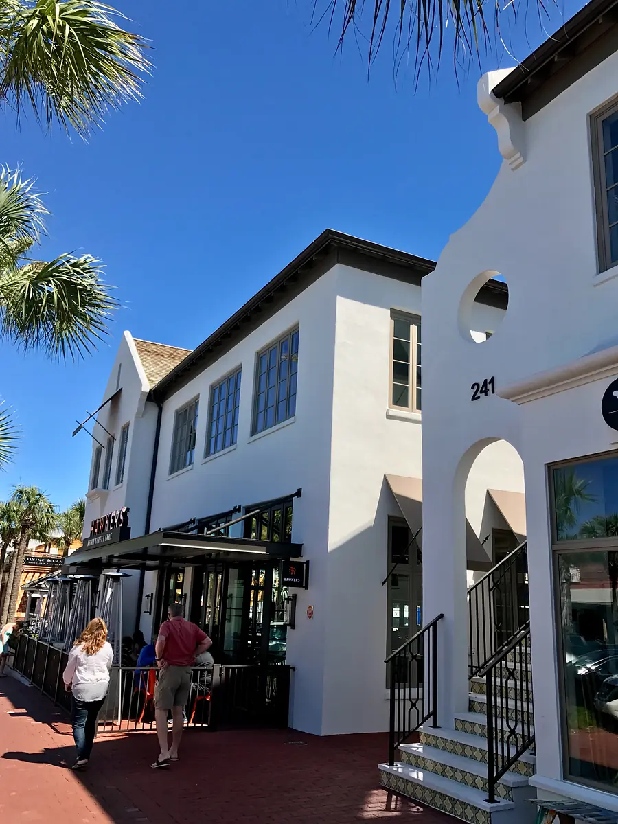 Exterior front of a two-story building with large windows, white stucco, and palm trees.
