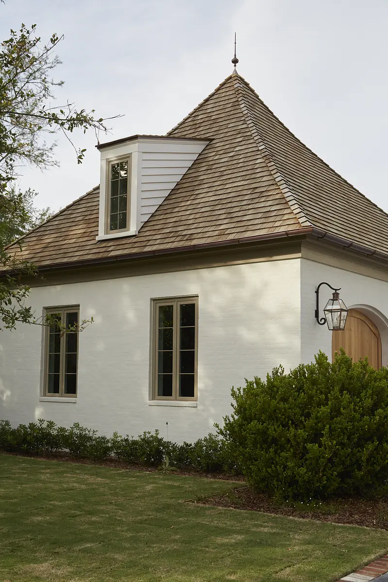 Exterior view of a building with steep roof, white brick, wooden siding, windows, door, and landscaped area.